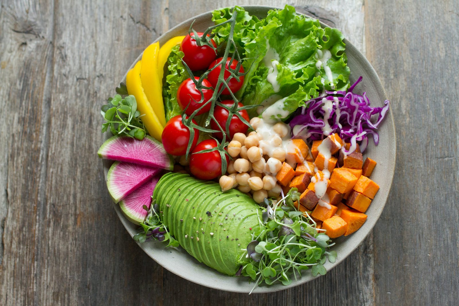 A colorful bowl of fresh vegetables, greens, avocado and tomatoes